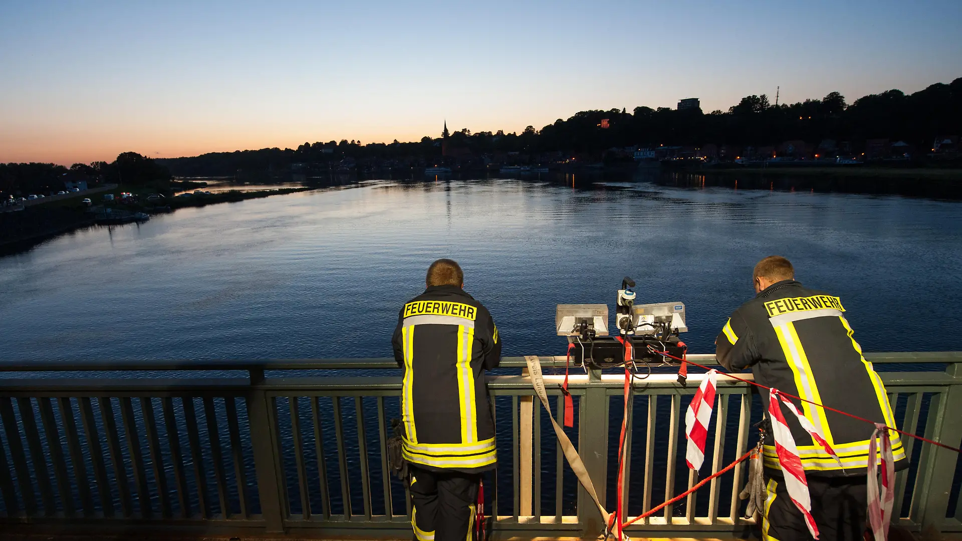 Einsatzkräfte der Feuerwehr stehen am 31.07.2015 bei Hohnstorf/Elbe (Niedersachsen) auf einer Brücke die über die Elbe nach Lauenburg (Schleswig-Holstein) führt. Im Fall der verschwundenen Familie aus Drage (Niedersachsen) prüft die Polizei einen Zusammenhang mit einer in der Elbe in Lauenburg gefundenen männlichen Leiche. Foto: Philipp Schulze/dpa | Verwendung weltweit