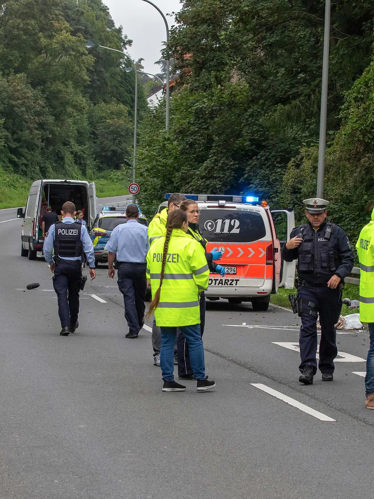 Polizisten stehen auf einer Straße in dem Ort bei Aachen, wo zuvor ein Kleintransporter eine Mutter und ihr Kind an einer Bushaltestelle erfasst und tödlich verletzt hatte.