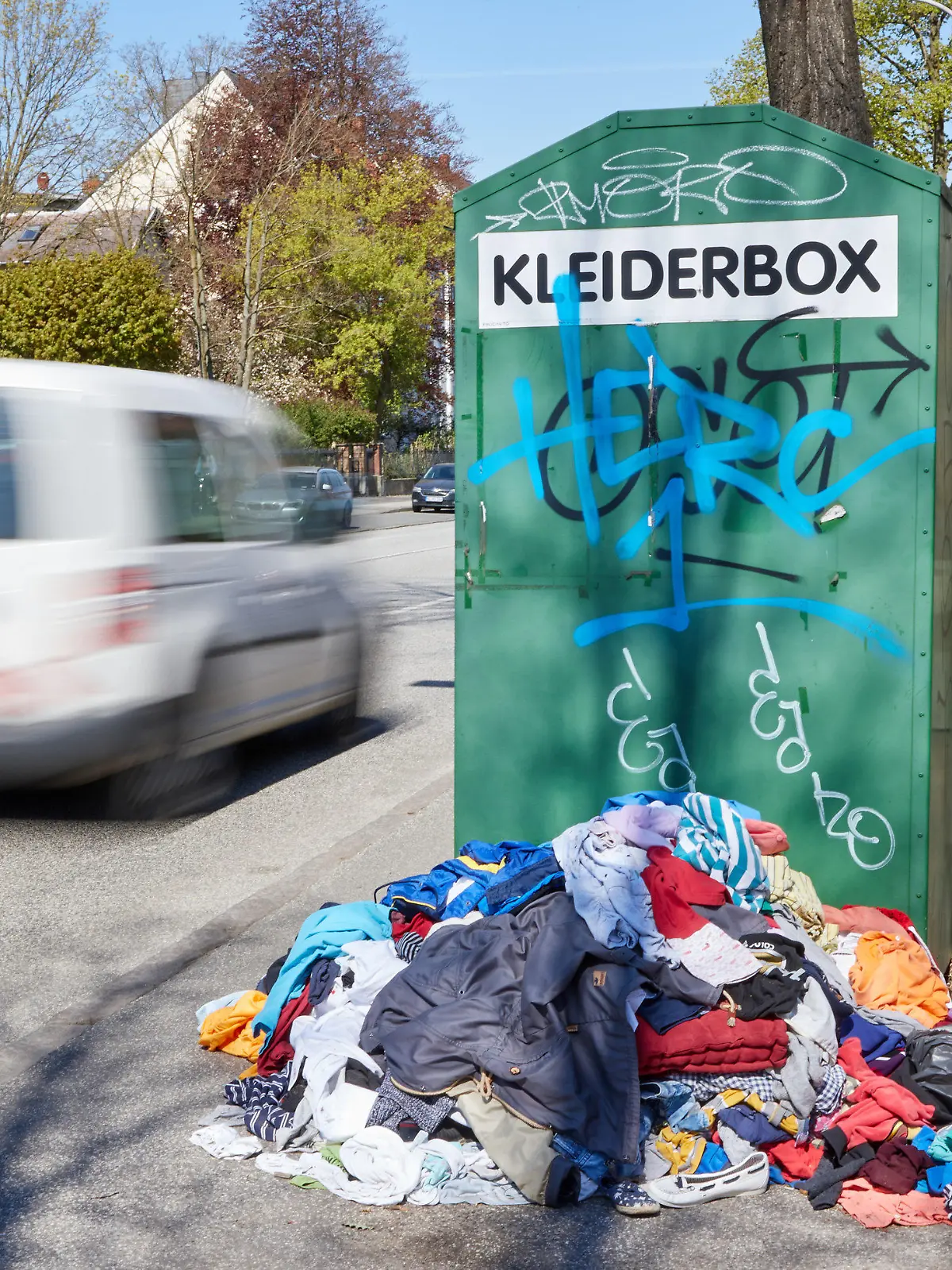 ARCHIV - 23.04.2020, Schleswig-Holstein, Lübeck: Ein Kleiderberg liegt vor einem Altkleidercontainer mit der Aufschrift «Kleiderbox» am Straßenrand. Der Kleiderschrank frisch sortiert, die ungeliebten Stücke in Säcken verstaut und in den Fächern wieder Platz für Neues: Weil viele Menschen in Deutschland die Corona-Zwangspause für ausgiebiges Ausmisten nutzten, gelangen Textil-Recycler an ihre Grenzen. (Wischeffekt durch Langzeitbelichtung) Foto: Georg Wendt/dpa +++ dpa-Bildfunk +++