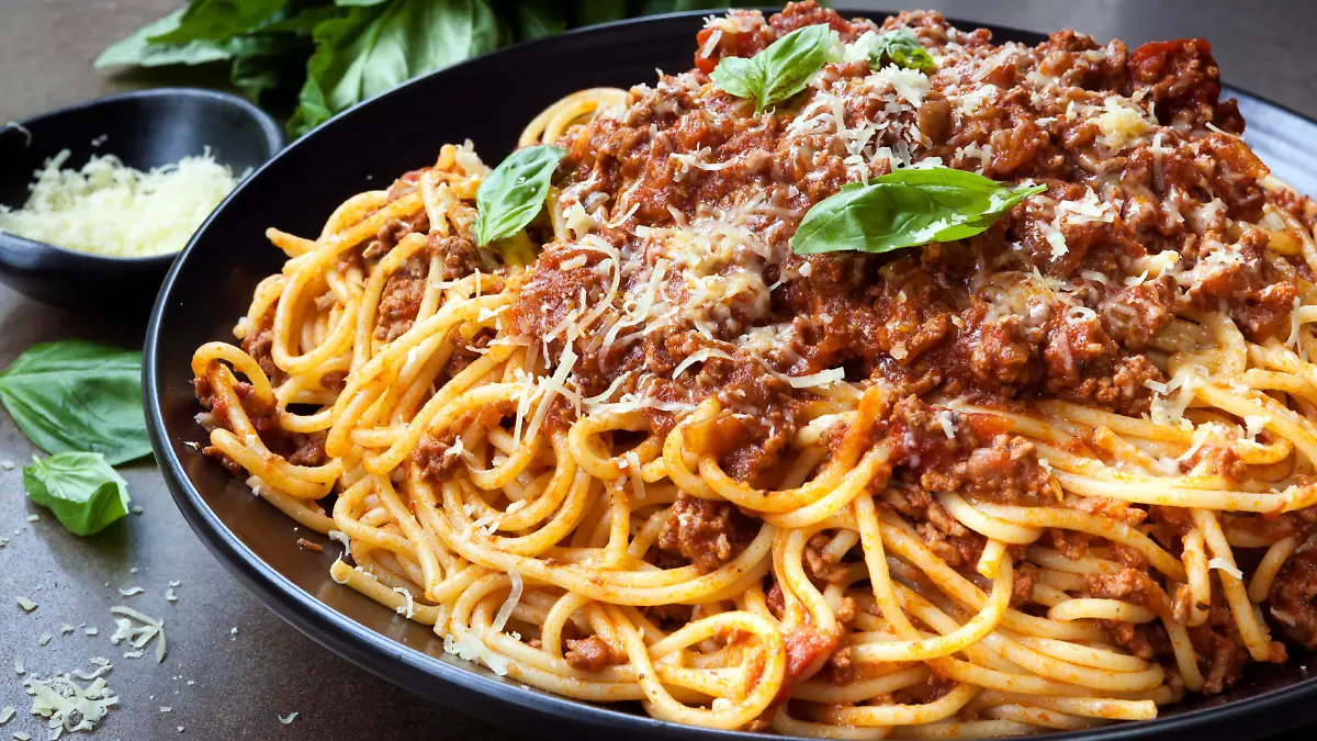 Spaghetti bolognese in black serving platter, with fresh basil and parmesan.
