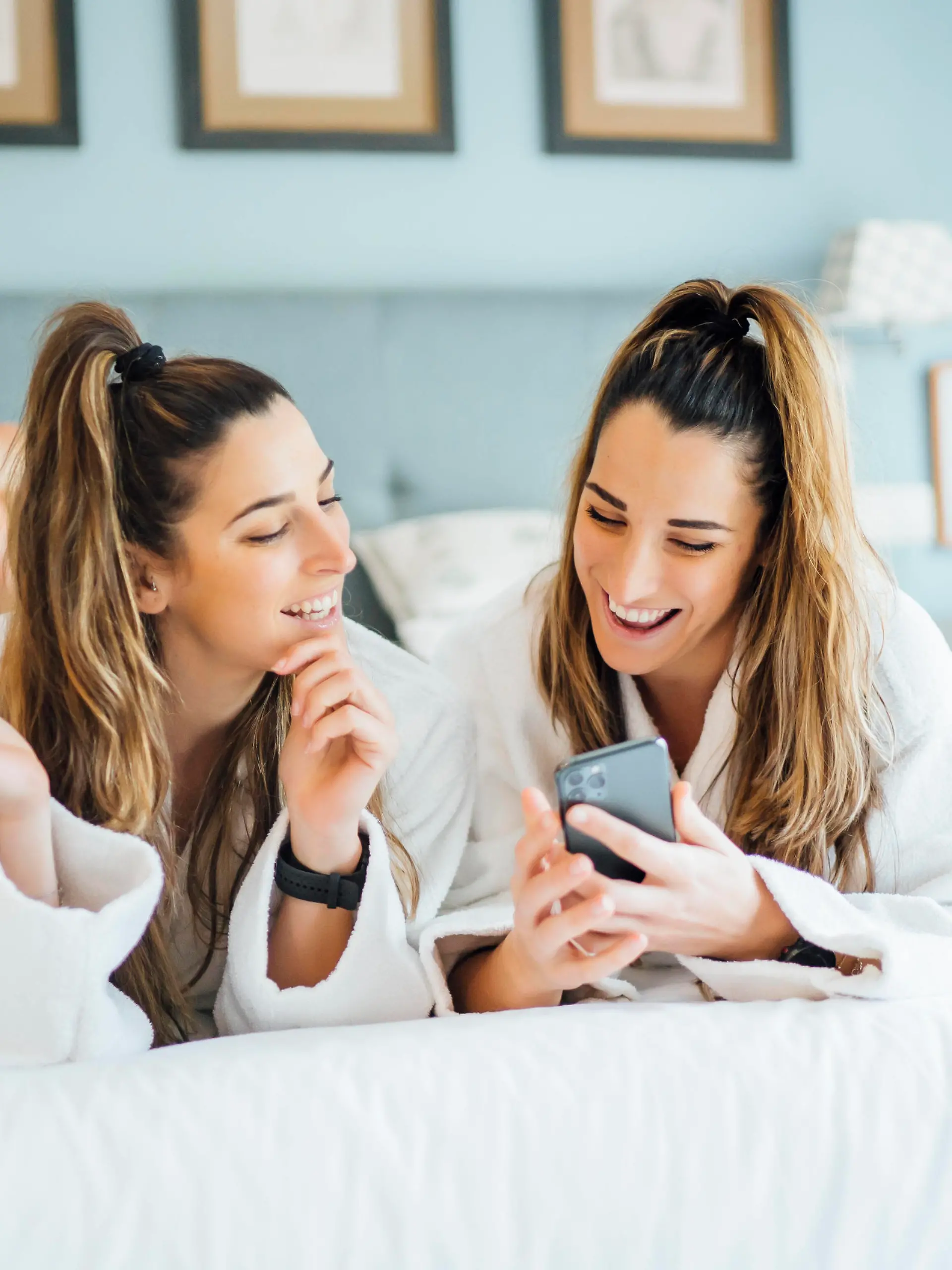  Smiling twin sisters using smart phone while lying on bed in hotel model released Symbolfoto property released OCMF01557