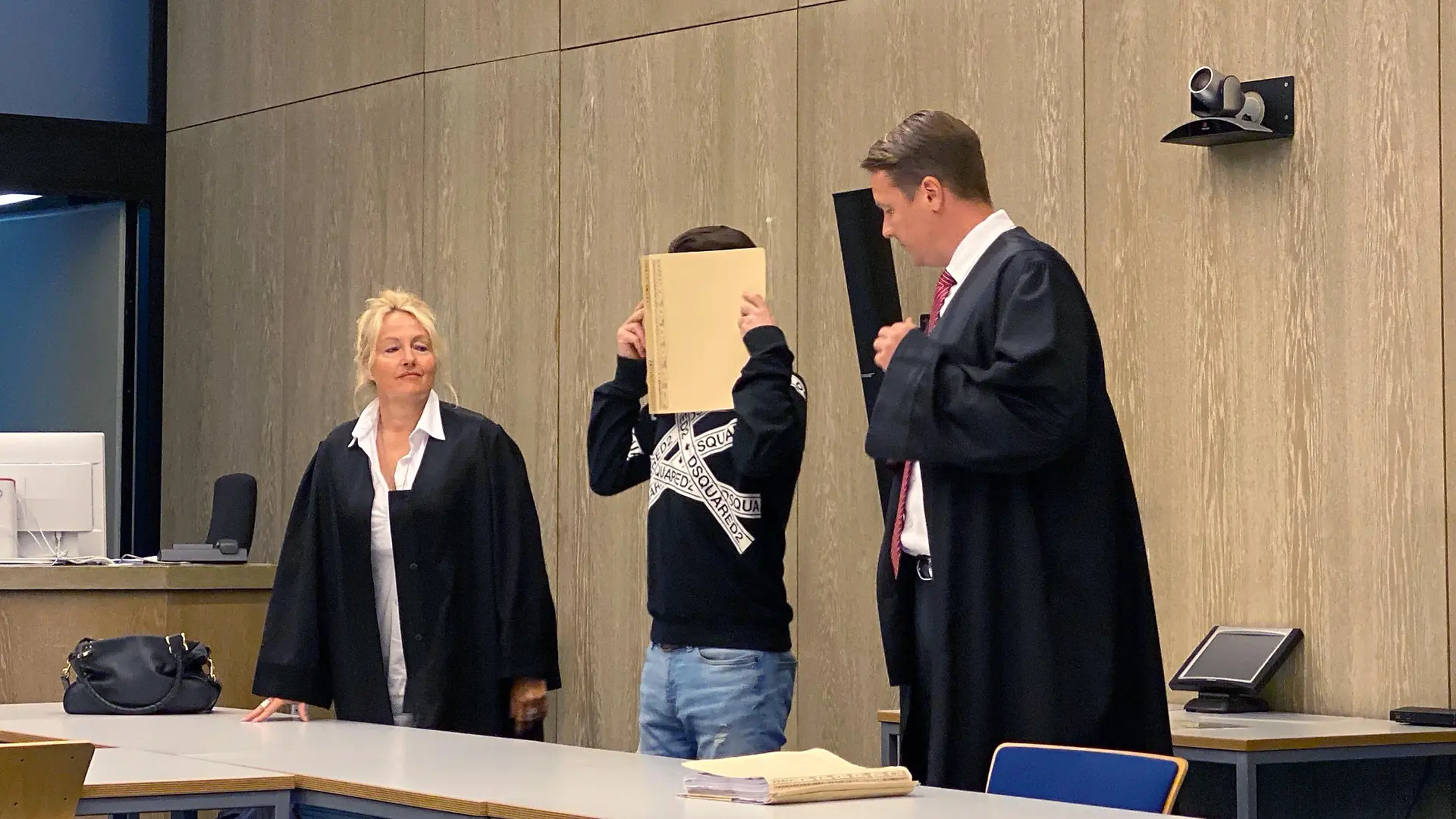 15.07.2020, Baden-Württemberg, Mannheim: Ein Angeklagter (M) steht vor Beginn der Urteilsverkündung mit einem Aktenordner vor dem Gesicht im Gerichtssaal zwischen seinen Anwälten Steffen Lindeberg (r) und Ute Mannebach-Junge (l). Nach einem tödlichen Angriff mit einem Hammer und einem Messer auf seine Ex-Freundin ist der 34-Jährige wegen Mordes zu lebenslanger Haft verurteilt worden. (zu dpa «Ex-Partnerin mit Hammer und Messer getötet - lebenslange Haft») Foto: Julian Weber/dpa | Verwendung weltweit