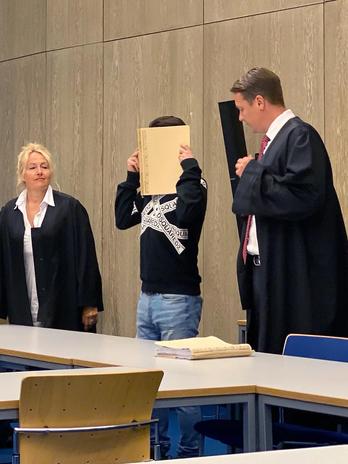 15.07.2020, Baden-Württemberg, Mannheim: Ein Angeklagter (M) steht vor Beginn der Urteilsverkündung mit einem Aktenordner vor dem Gesicht im Gerichtssaal zwischen seinen Anwälten Steffen Lindeberg (r) und Ute Mannebach-Junge (l). Nach einem tödlichen Angriff mit einem Hammer und einem Messer auf seine Ex-Freundin ist der 34-Jährige wegen Mordes zu lebenslanger Haft verurteilt worden. (zu dpa «Ex-Partnerin mit Hammer und Messer getötet - lebenslange Haft») Foto: Julian Weber/dpa | Verwendung weltweit