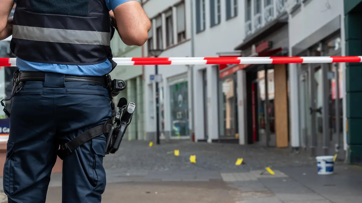19.08.2023, Saarland, Wittlich: Ein Polizist sichert die Stelle in der Strasse, in der in der Nacht auf Samstag ein junger Mann getötet worden ist. Foto: Harald Tittel/dpa +++ dpa-Bildfunk +++