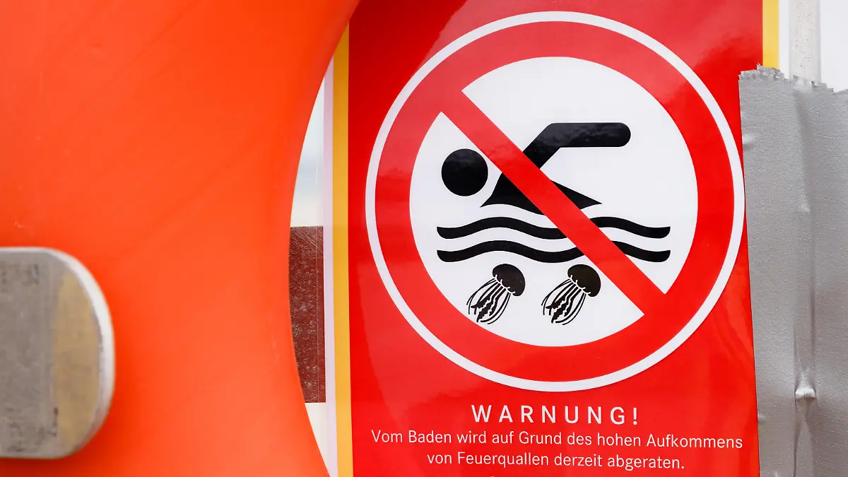 17.08.2018, Schleswig-Holstein, Travemünde: Ein Zettel mit der Aufschrift «Warnung! Vom Baden wird auf Grund des hohen Aufkommens von Feuerquallen derzeit abgeraten» warnt an einem Rettungsring vor dem Baden in der Ostsee. Foto: Markus Scholz/dpa