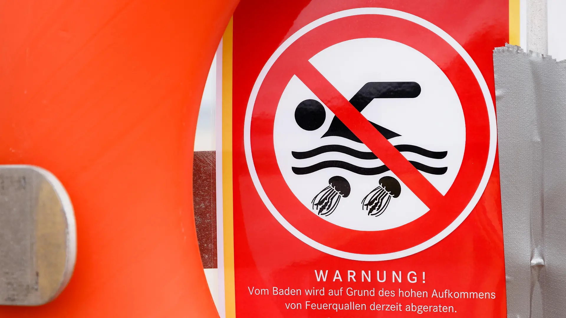 17.08.2018, Schleswig-Holstein, Travemünde: Ein Zettel mit der Aufschrift «Warnung! Vom Baden wird auf Grund des hohen Aufkommens von Feuerquallen derzeit abgeraten» warnt an einem Rettungsring vor dem Baden in der Ostsee. Foto: Markus Scholz/dpa