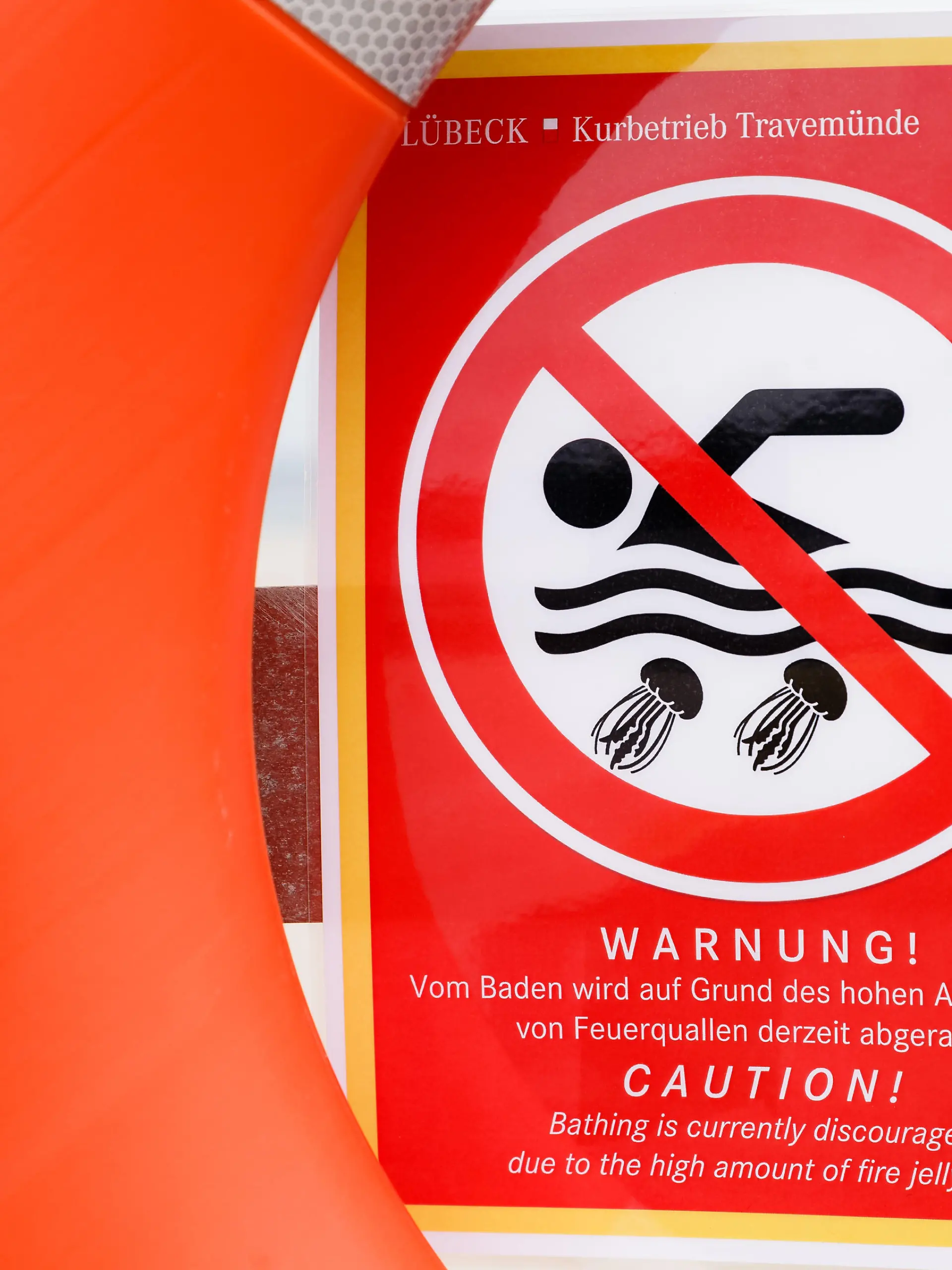 17.08.2018, Schleswig-Holstein, Travemünde: Ein Zettel mit der Aufschrift «Warnung! Vom Baden wird auf Grund des hohen Aufkommens von Feuerquallen derzeit abgeraten» warnt an einem Rettungsring vor dem Baden in der Ostsee. Foto: Markus Scholz/dpa