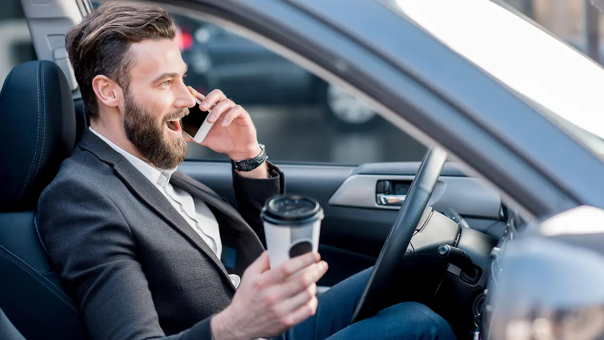 Mann fährt im Auto mit Kaffee und Handy