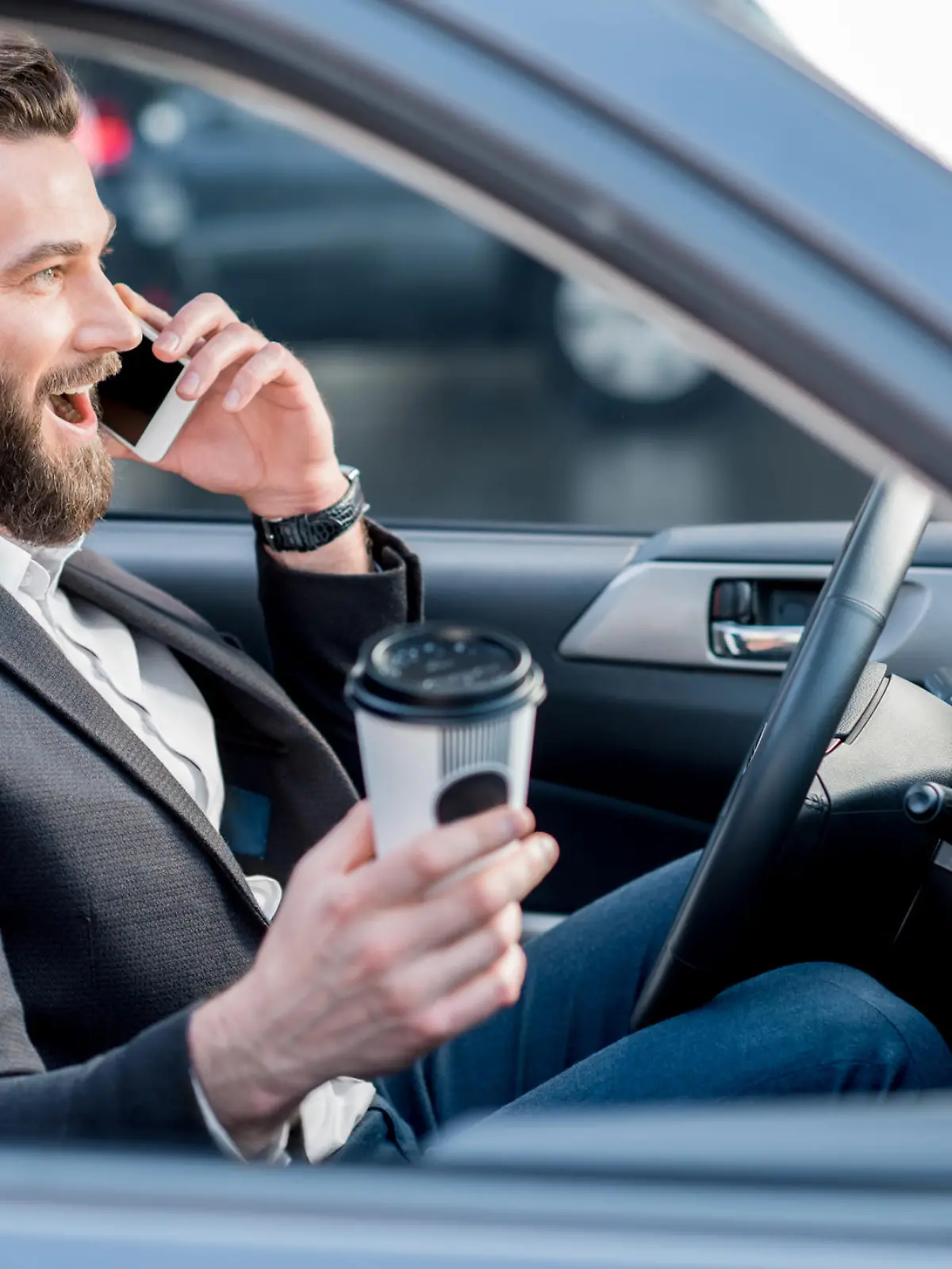 Mann fährt im Auto mit Kaffee und Handy