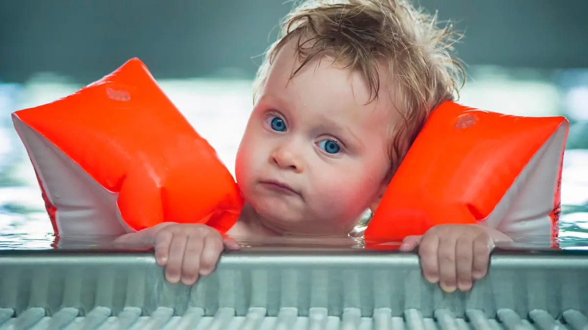 Baby boy makes face in a swiming pool. DOF focus on babys and mother face with defocused background.