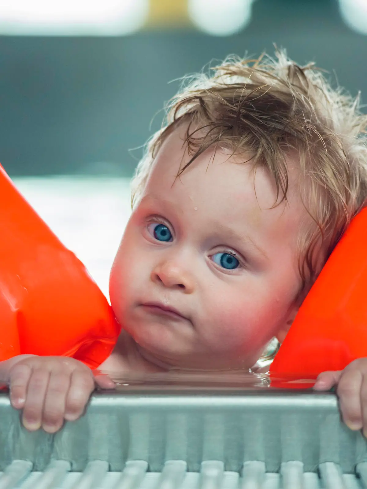 Baby boy makes face in a swiming pool.  DOF focus on babys and mother face with  defocused background.