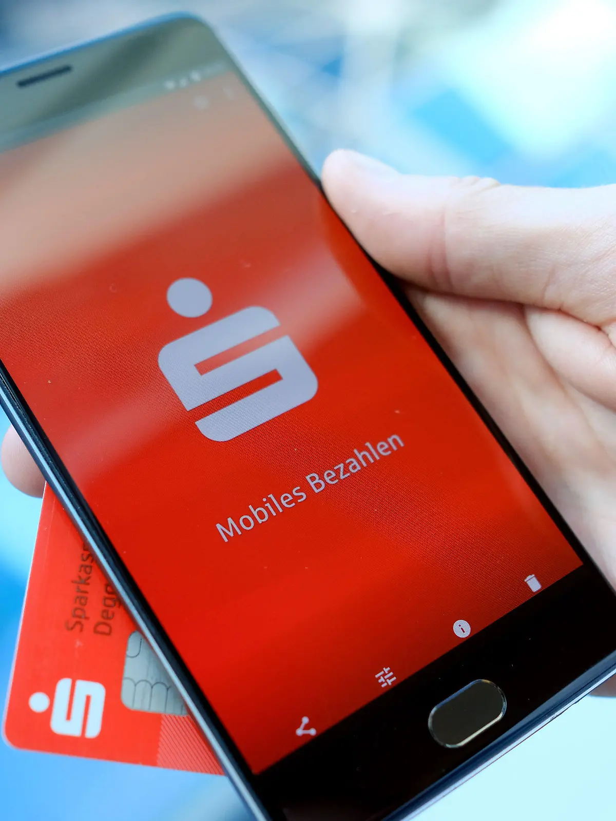 ILLUSTRATION - 30.07.2018, Berlin: Ein Mann hält eine EC-Karte und ein Mobiltelefon, auf dem der Startbildschirm der Mobiles Bezahlen - App der Sparkasse dargestellt wird, in der Hand. Mit dem Smartphone statt Bankkarte an der Ladenkasse zahlen können inzwischen - zumindest technisch gesehen - viele in Deutschland. Foto: Fabian Sommer/dpa +++ dpa-Bildfunk +++