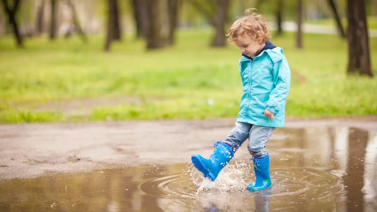 Kleiner Junge in beschichteter Outdoor-Jacke spielt in Pfütze