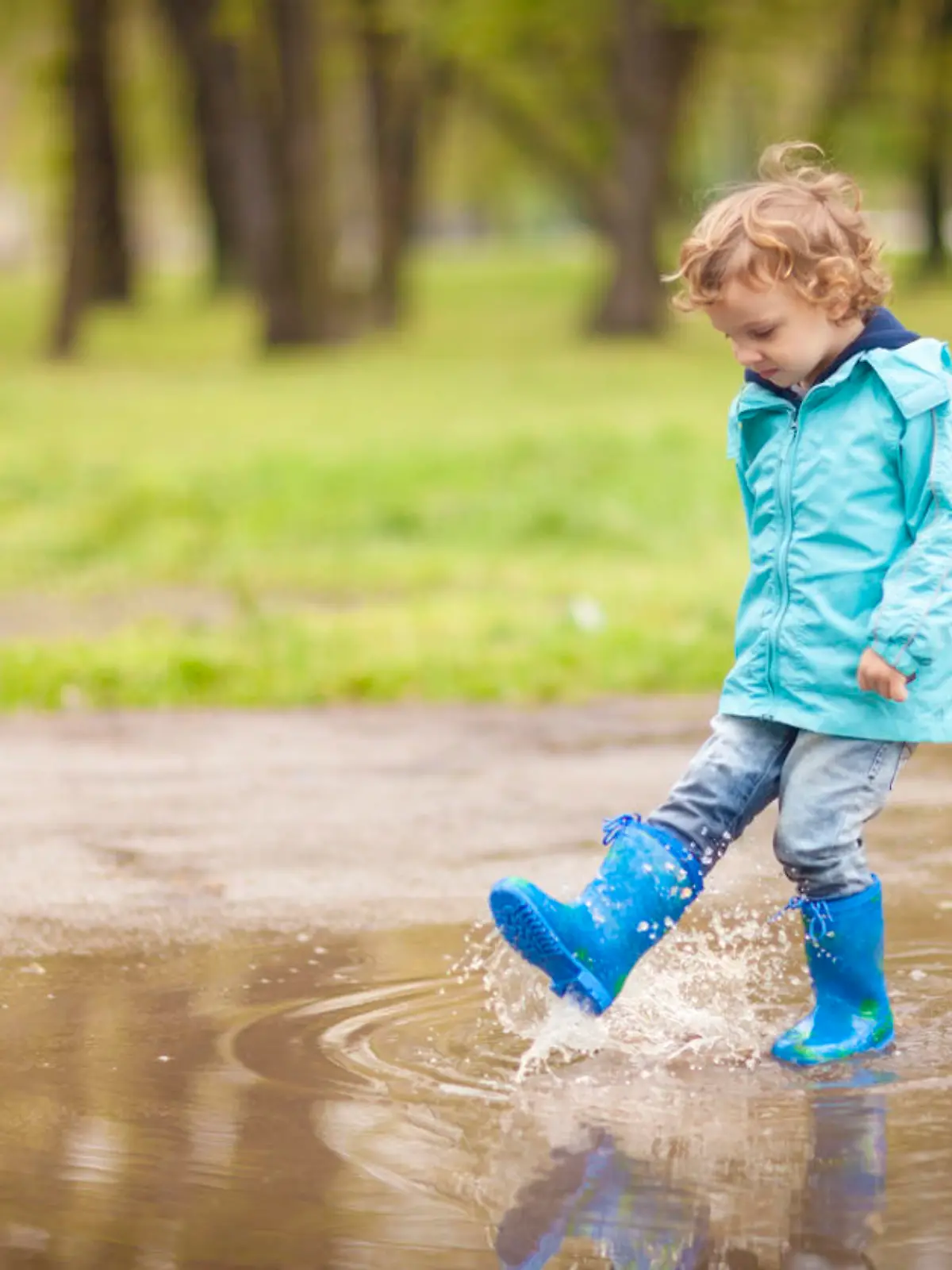 Kleiner Junge in beschichteter Outdoor-Jacke spielt in Pfütze