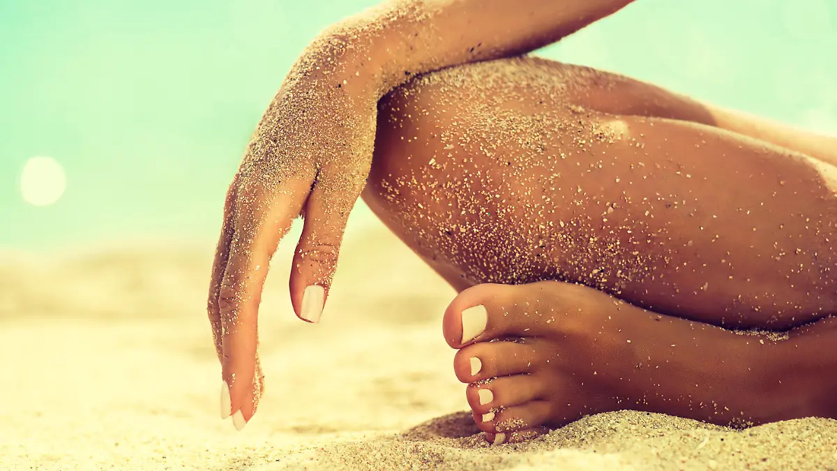 Body parts, Womans hand is laying on the covered by sea sand knee. Symbol of rest and relaxation on tropical beach. Tanned girl in Lotus position yoga and meditation.