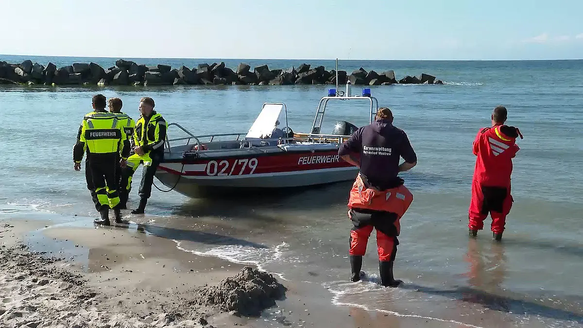 01.07.2020, Mecklenburg-Vorpommern, Ahrenshoop: Rettungskräfte stehen am Strand neben einem Boot. Am Strand von Ahrenshoop auf der Halbinsel Fischland-Darß-Zingst hat ein Mann am Mittwoch zwei Kindern beim Baden das Leben gerettet und ist selbst gestorben. Der 32-Jährige aus der Region war nach Polizeiangaben im Wasser verschwunden, nachdem er zwei Zehnjährige auf eine Steinmole gehievt hatte. Foto: Stefan Tretropp/dpa +++ dpa-Bildfunk +++