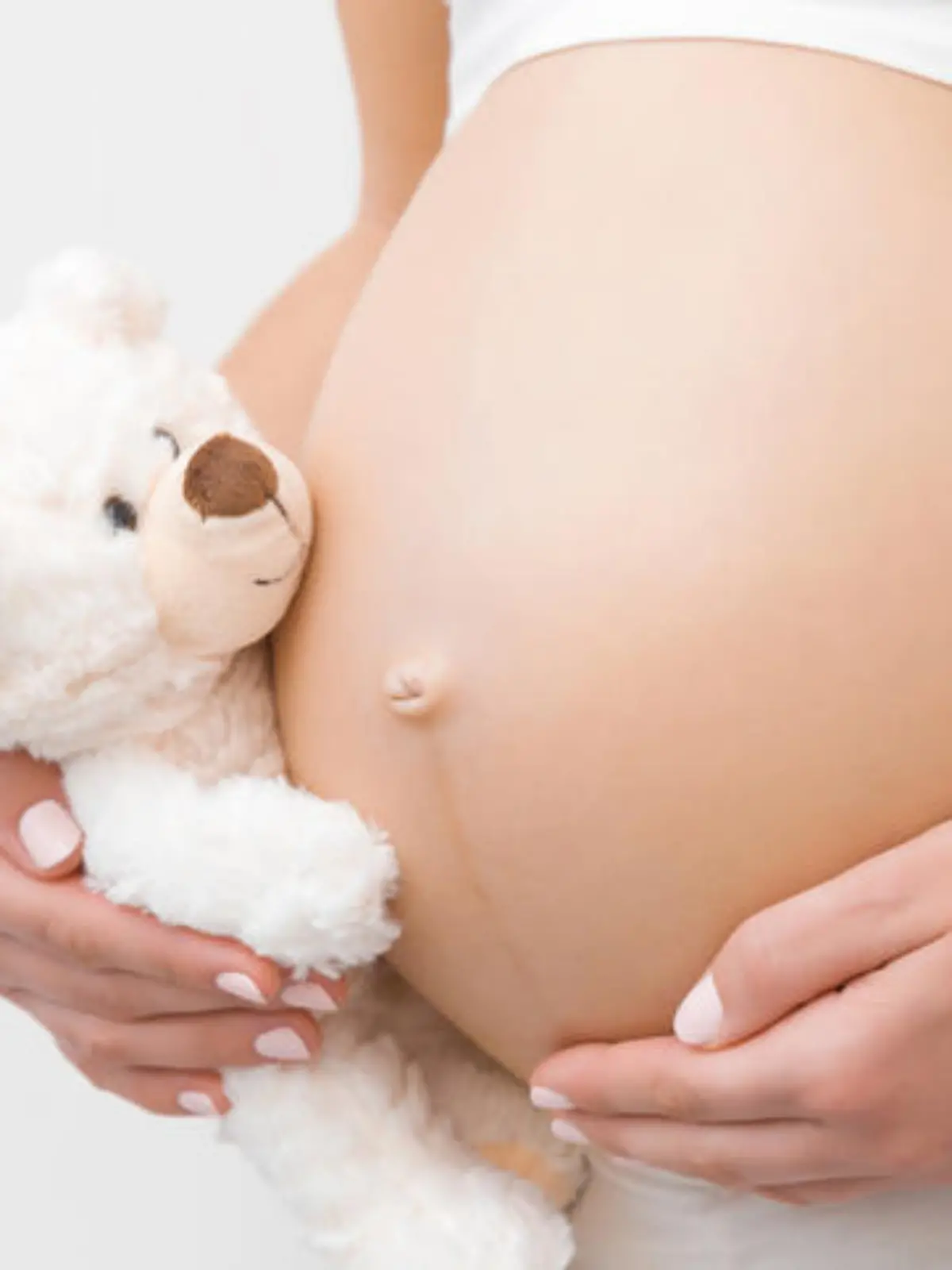 schwangerer Teenager hält sich den Babybauch und hat einen Plüschteddy in der Hand
