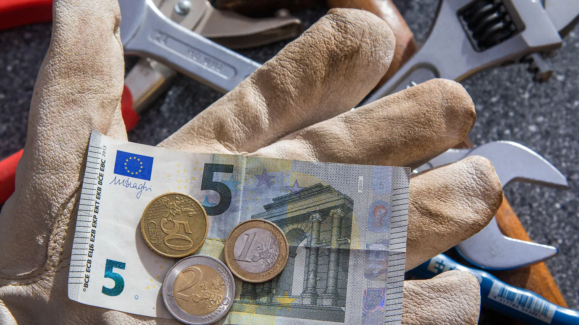 ARCHIV - ILLUSTRATION - Auf einer Hand mit einem Arbeitshandschuh sind am 26.02.2015 in Schwerin (Mecklenburg-Vorpommern) Euromünzen und einem Fünf-Euro-Geldschein mit einem Betrag von 8,50 Euro zu sehen (gestelltes Foto). Foto: Jens Büttner/dpa (zu dpa «IAB-Chef: Mindestlohn-Erhöhung kein Risiko für den Arbeitsmarkt» vom 23.06.2016) +++(c) dpa - Bildfunk+++