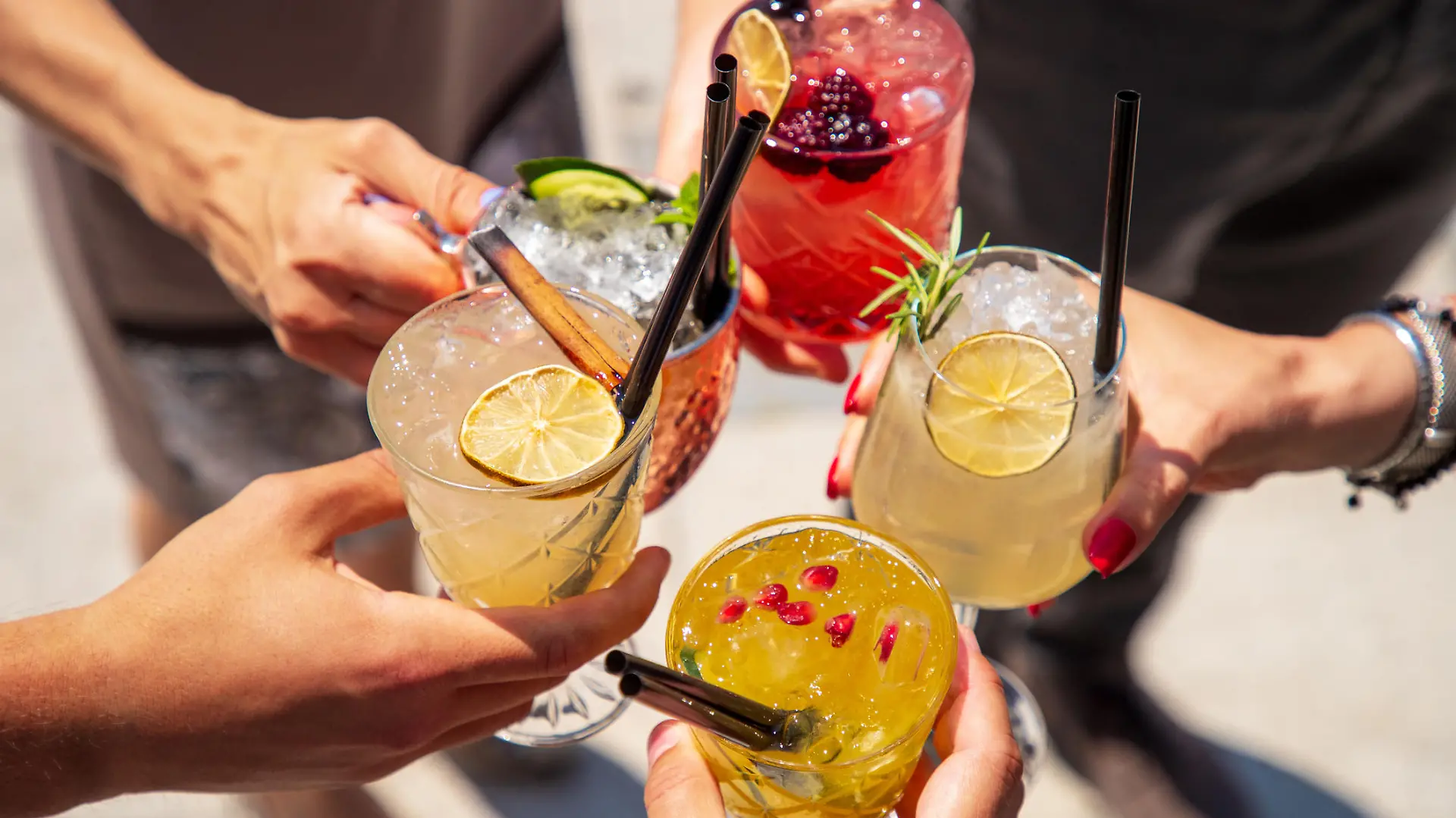 Five exotic cocktails on ice in hands joined in celebratory toast