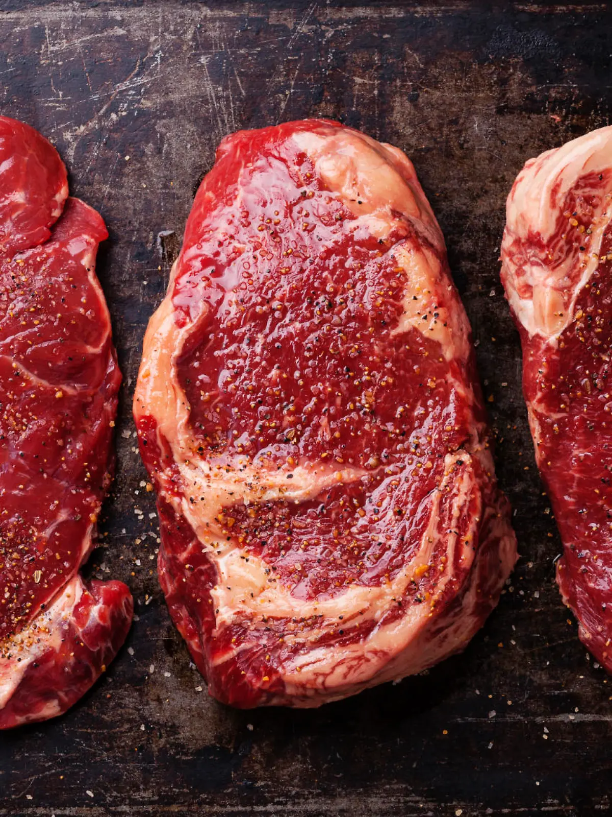 Three cuts of Raw fresh meat Steaks and seasonings on dark background