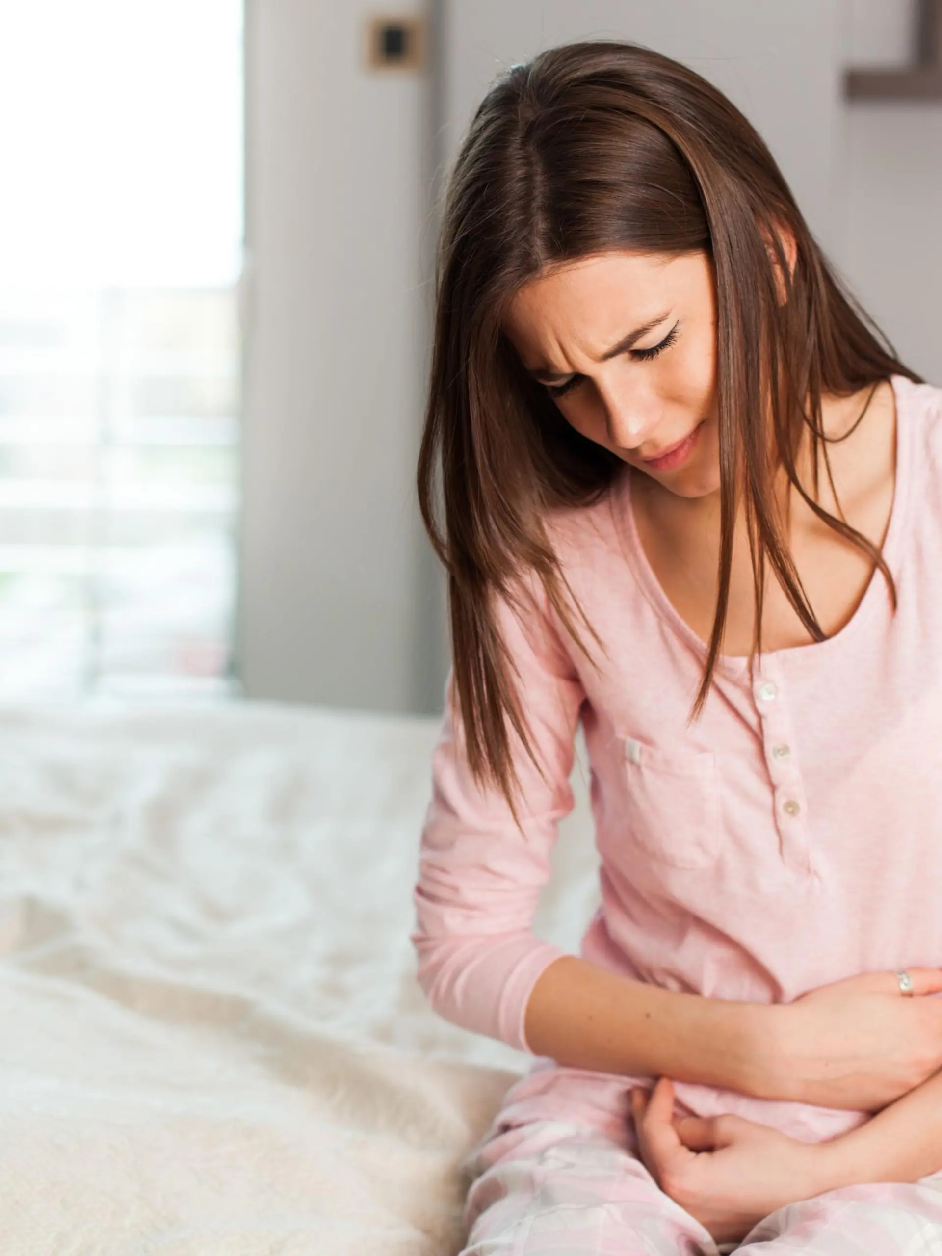 Young woman with a stomach ache in the bedroom, sitting holding her abdomen