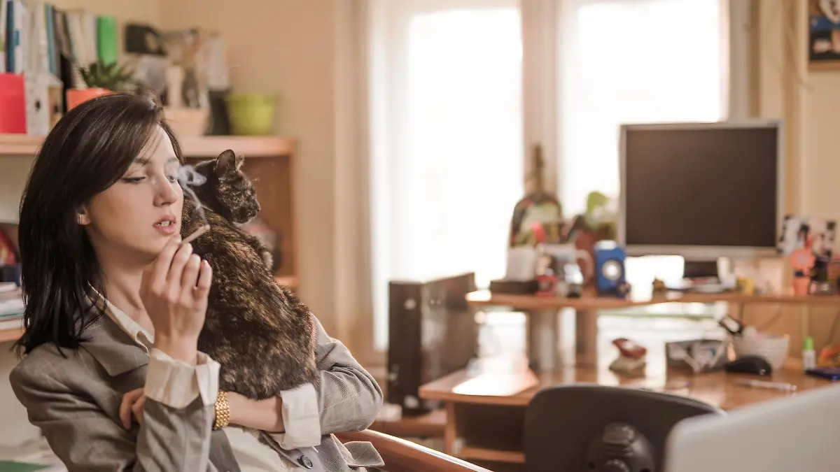 Junge Frau hat Katze auf dem Arm und raucht dabei eine Zigarette 