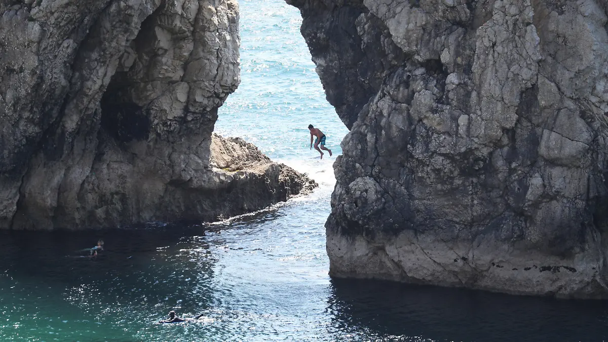 31.05.2020, Großbritannien, Lulworth: Ein Mann springt von der Durdle Door, einer natürlichen Felsbrücke aus Kalkstein, ins Meer, obwohl der Gemeinderat von Dorset den Strand für die Öffentlichkeit geschlossen hat, nachdem sich drei Menschen bei Sprüngen von den Felsen schwer verletzt hatten. Foto: Andrew Matthews/PA Wire/dpa +++ dpa-Bildfunk +++