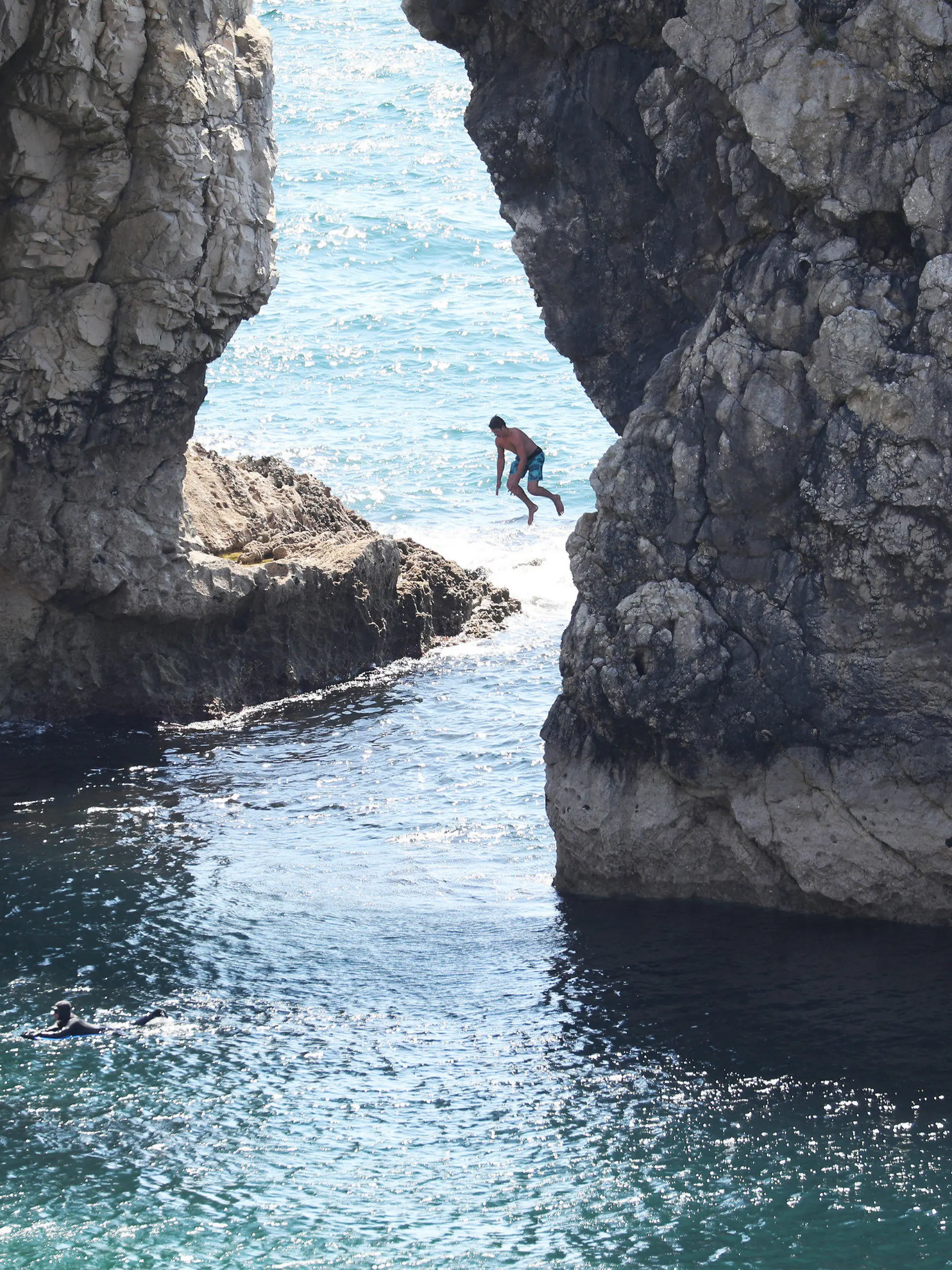 31.05.2020, Großbritannien, Lulworth: Ein Mann springt von der Durdle Door, einer natürlichen Felsbrücke aus Kalkstein, ins Meer, obwohl der Gemeinderat von Dorset den Strand für die Öffentlichkeit geschlossen hat, nachdem sich drei Menschen bei Sprüngen von den Felsen schwer verletzt hatten. Foto: Andrew Matthews/PA Wire/dpa +++ dpa-Bildfunk +++