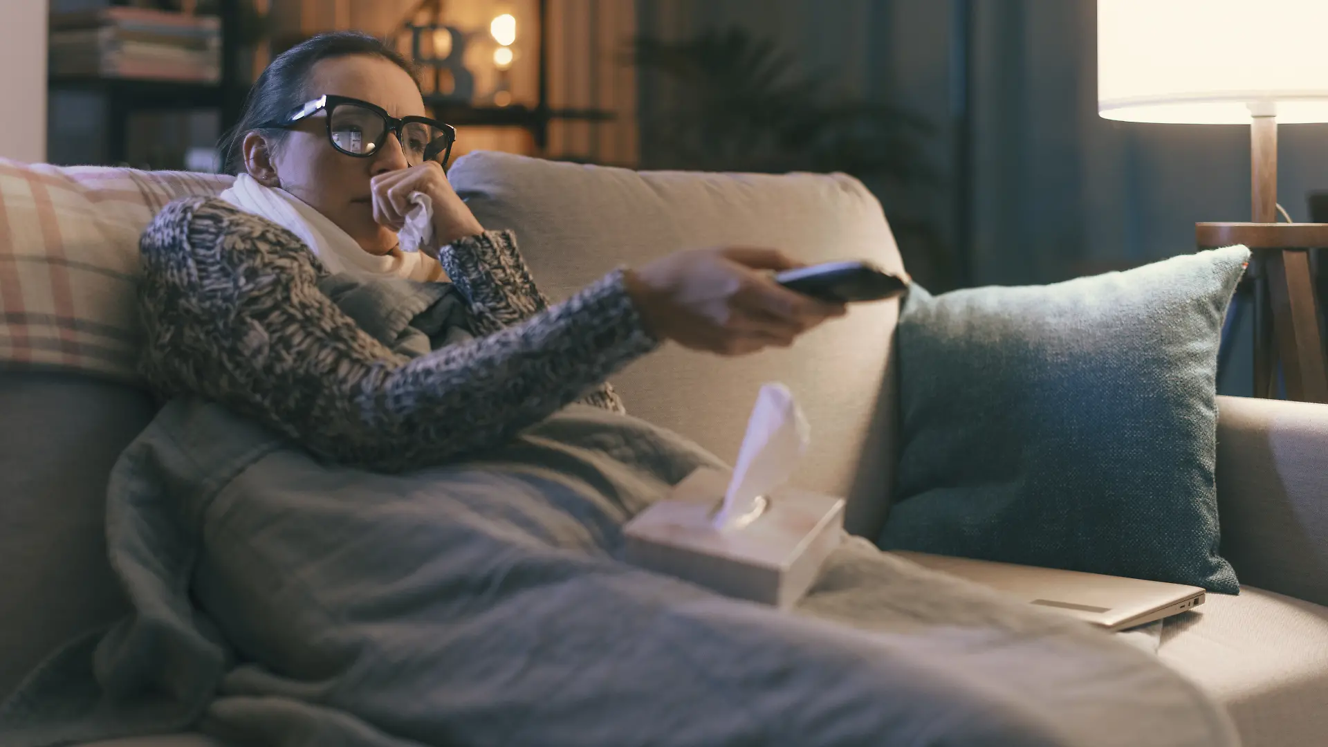 Junge Frau sitzt krank auf der Couch.