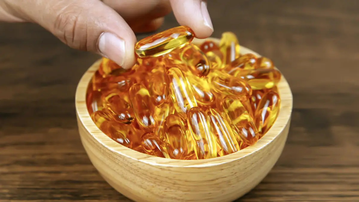 Hand picked cod liver oil capsule or fish oil in a wooden cup. Dietary supplement for health-care concepts.