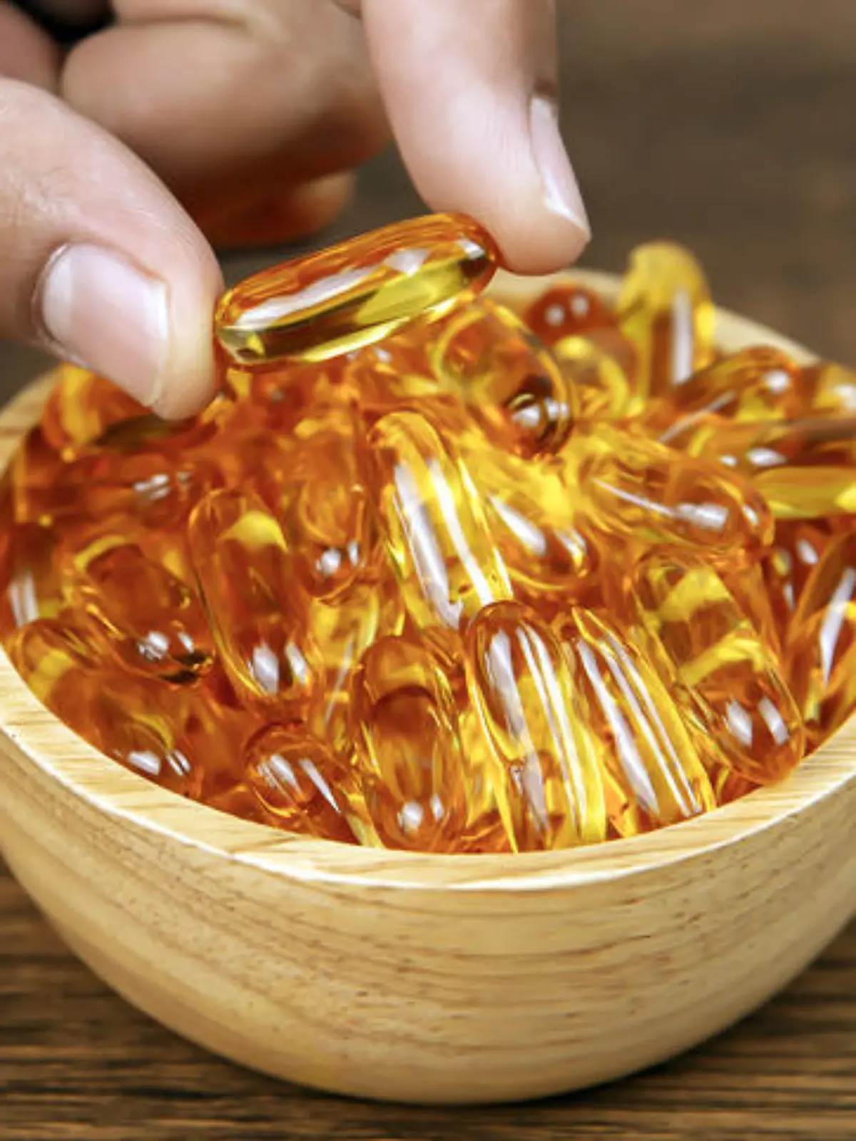 Hand picked cod liver oil capsule or fish oil in a wooden cup. Dietary supplement for health-care concepts.
