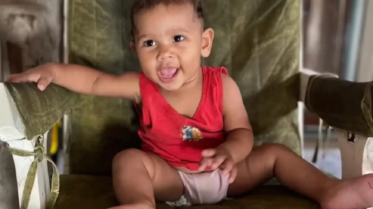 Ein baby sitzt auf einem Sessel und grinst fröhlich in die Kamera. 