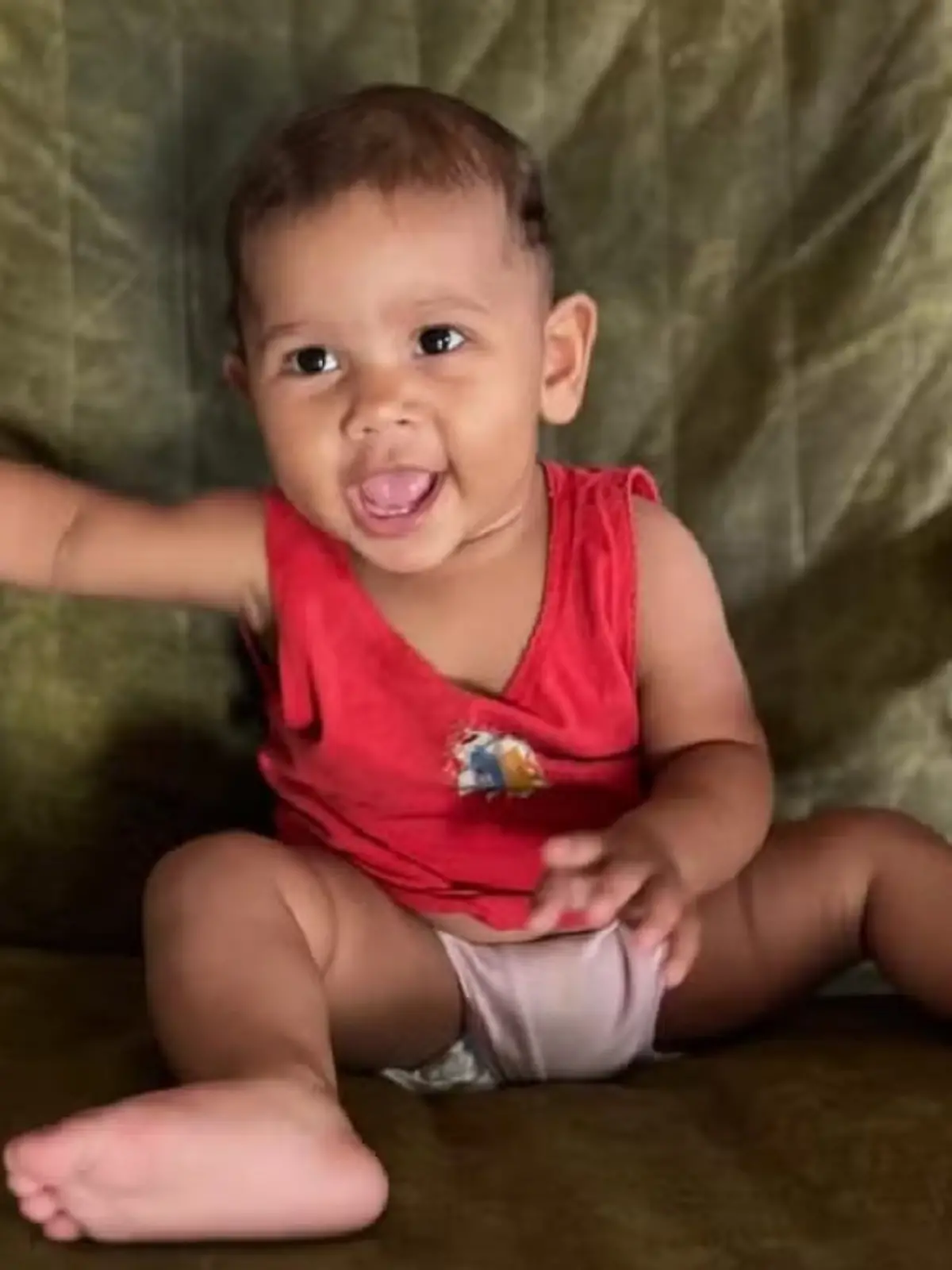Ein baby sitzt auf einem Sessel und grinst fröhlich in die Kamera. 