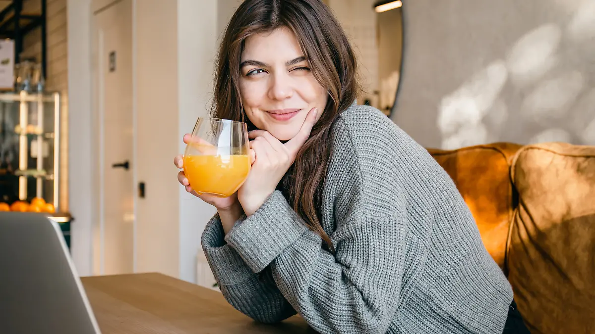 Eine glückliche junge Frau trinkt ein Glas Orangensaft.