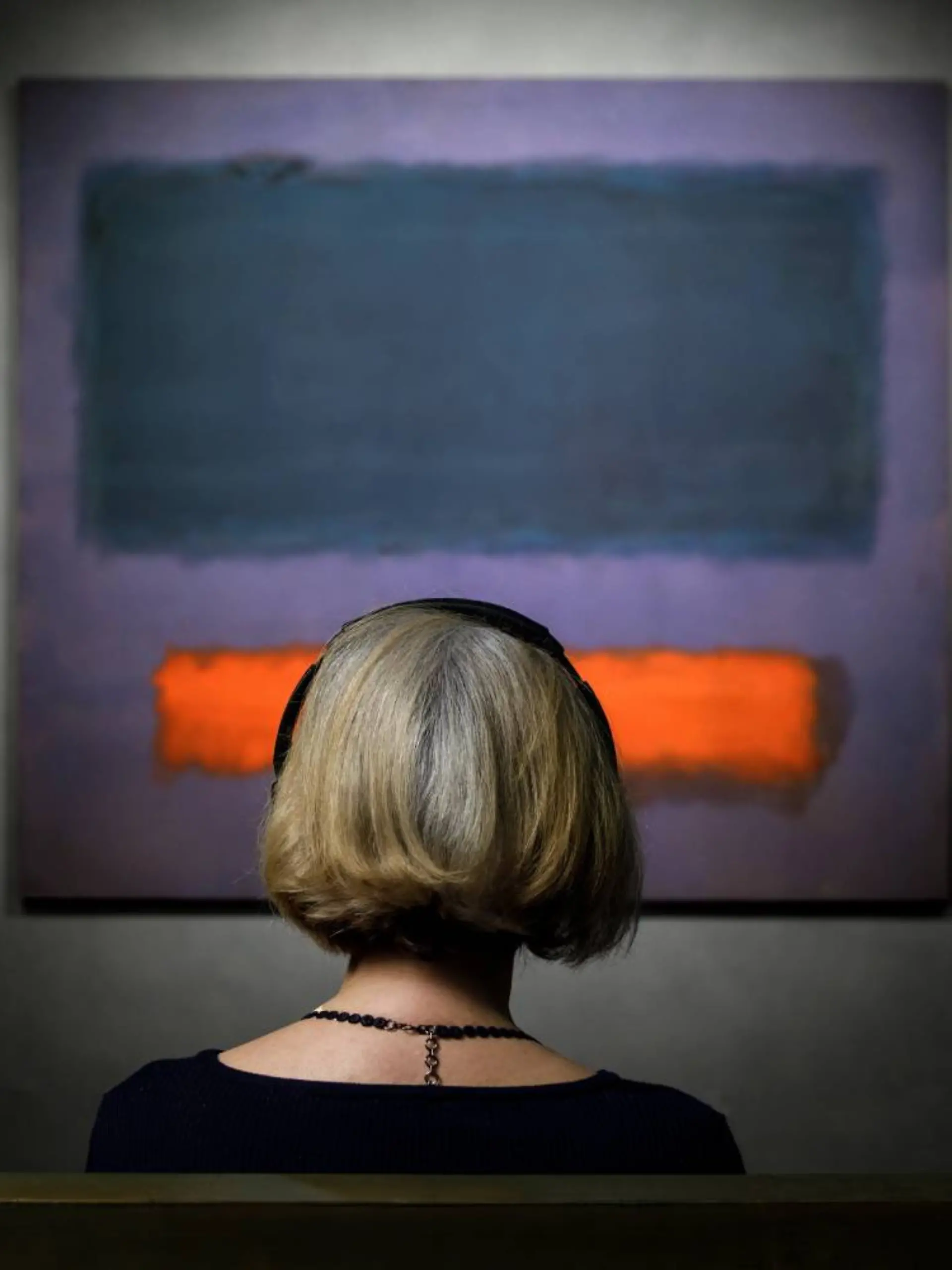 Frau sitzt vor dem Gemälde „Grey, Orange on Maroon, No. 8” 