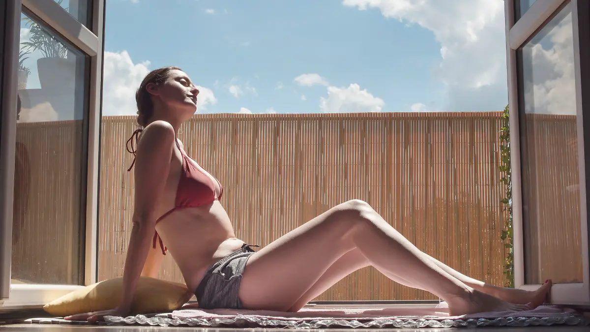 Frau sonnt sich im Bikini auf dem Balkon.