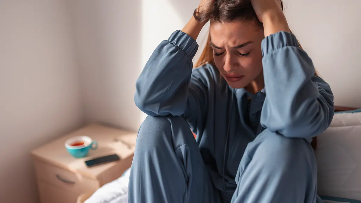 Eine junge Frau sitzt auf dem Bett und scheint gestresst zu sein.
