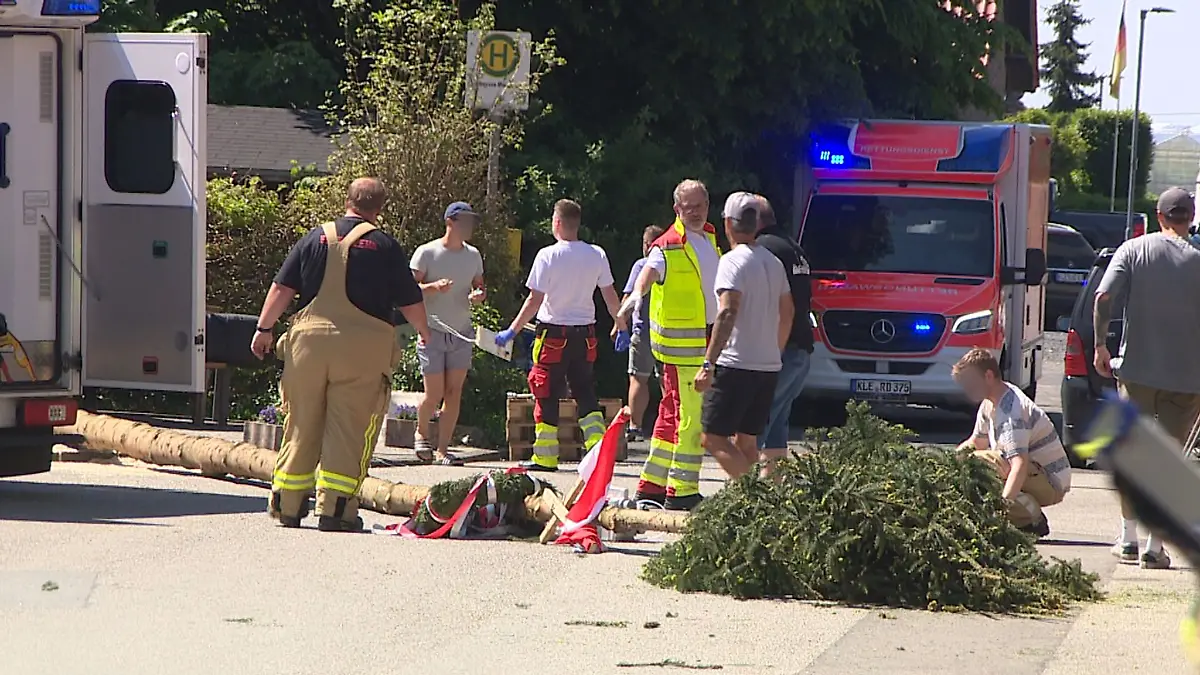 Der umgestürzte Maibaum liegt auf der Straße vor einem Einsatzwagen der Feuerwehr.