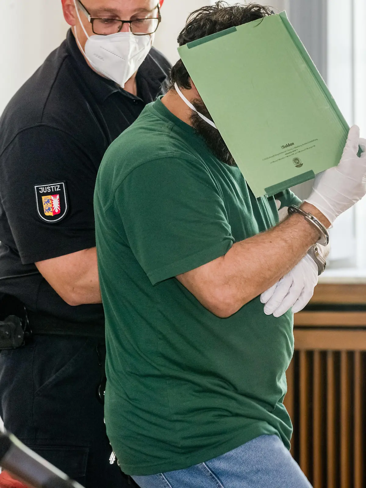 15.05.2020, Schleswig-Holstein, Lübeck: Der Angeklagte im Prozess um die Verschleppung und Vergewaltigung einer Studentin verbirgt im Gerichtssaal sein Gesicht hinter einem Aktendeckel. Er soll sein Opfer im Oktober 2019 entführt und nach der Tat auf einem einsamen Feldweg ausgesetzt haben. Er muss sich wegen versuchten Mordes, Vergewaltigung und Freiheitsberaubung vor dem Landgericht Lübeck verantworten. Foto: Markus Scholz/dpa +++ dpa-Bildfunk +++