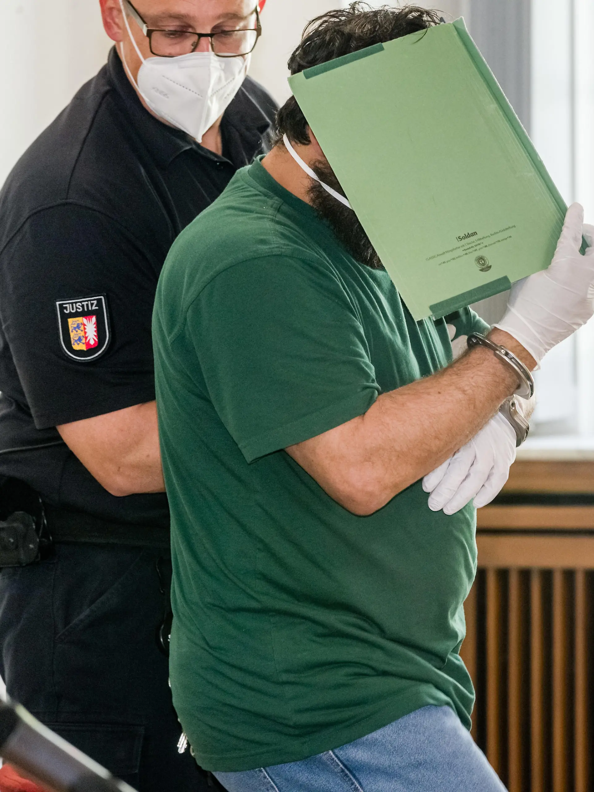 15.05.2020, Schleswig-Holstein, Lübeck: Der Angeklagte im Prozess um die Verschleppung und Vergewaltigung einer Studentin verbirgt im Gerichtssaal sein Gesicht hinter einem Aktendeckel. Er soll sein Opfer im Oktober 2019 entführt und nach der Tat auf einem einsamen Feldweg ausgesetzt haben. Er muss sich wegen versuchten Mordes, Vergewaltigung und Freiheitsberaubung vor dem Landgericht Lübeck verantworten. Foto: Markus Scholz/dpa +++ dpa-Bildfunk +++