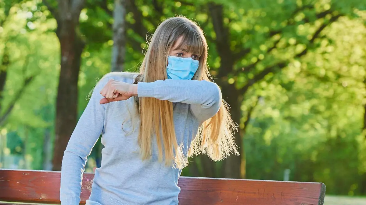 Frau mit Maske niest auf Bank