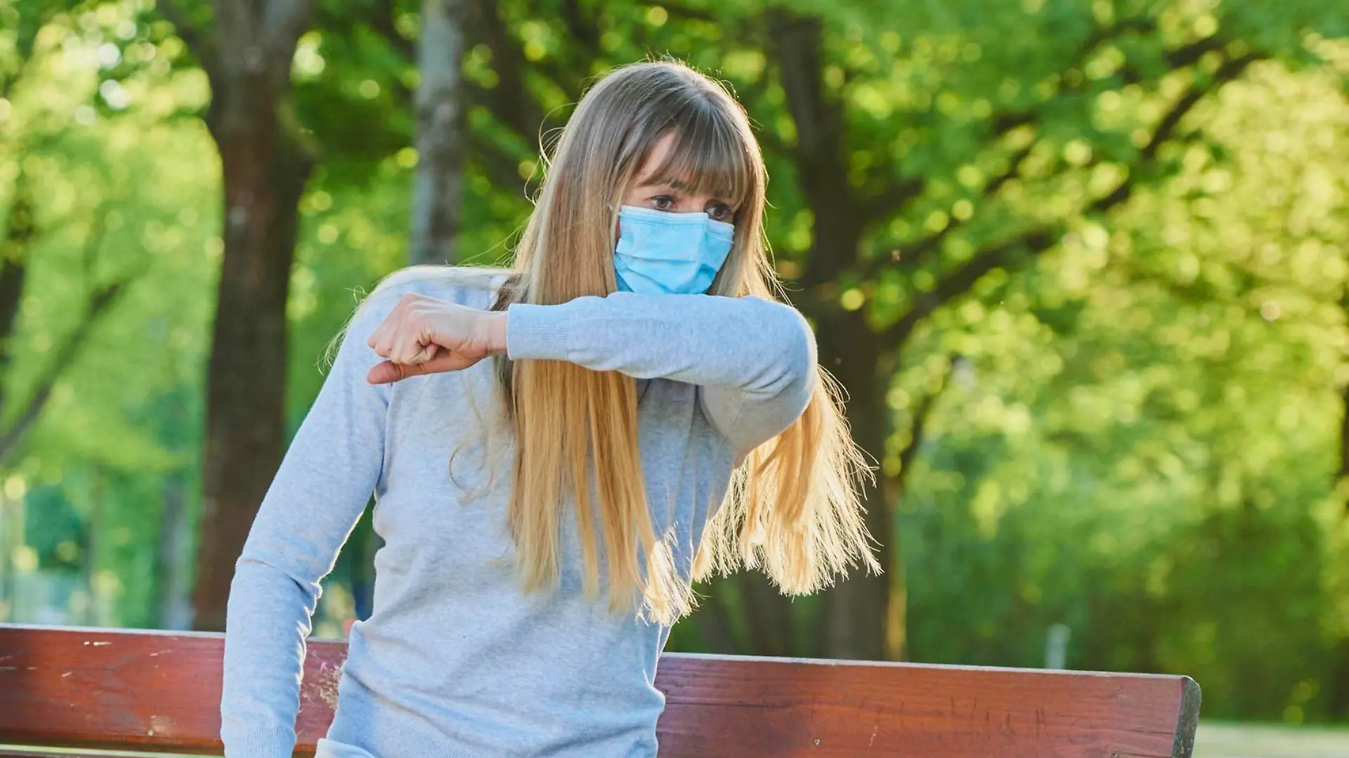 Frau mit Maske niest auf Bank