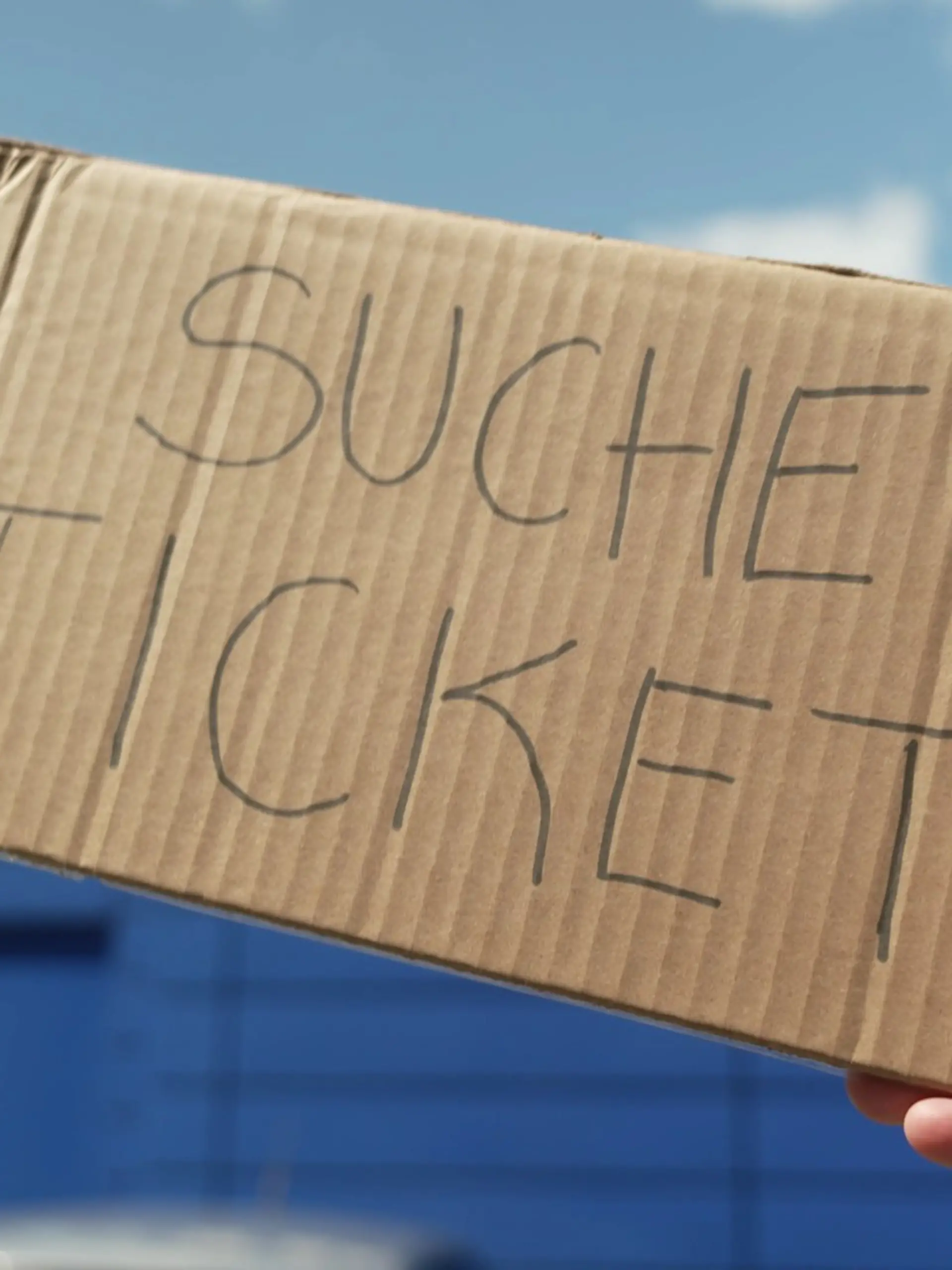 Eine Hand hält ein Pappschild mit der Aufschrift „Suche Ticket”