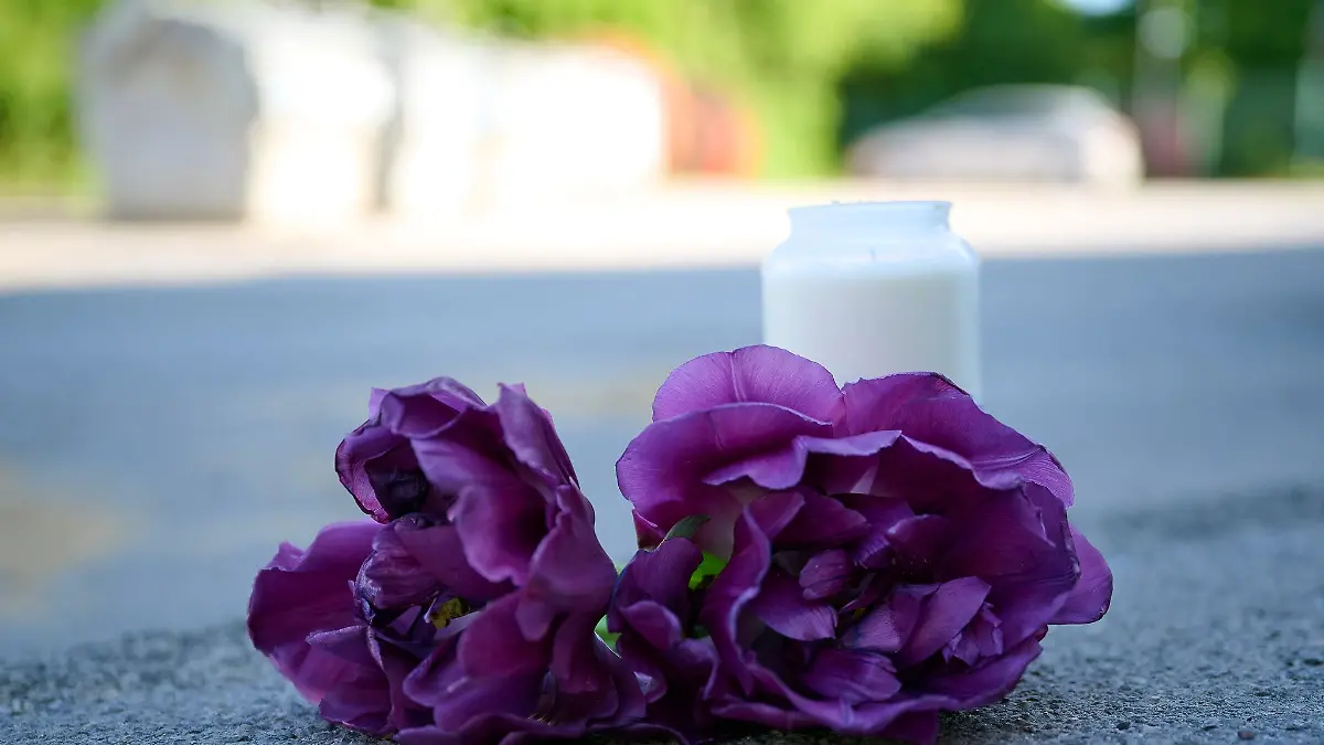 Blumen und eine Kerze liegen auf einem Schotterplatz vor dem Eingang zum Spielplatz, auf dem in der Nacht ein 17-Jähriger einen 14-Jährigen erstochen haben soll.