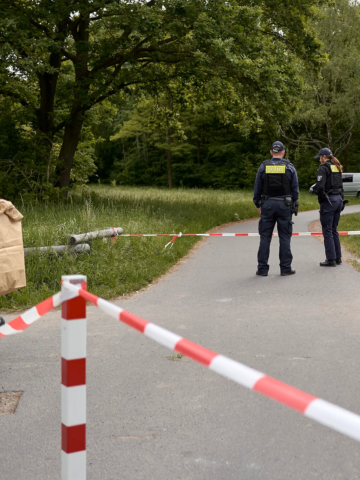 Einsatzkräfte der Polizei stehen hinter einer Absperrung an einem Weg im Stadtteil Gropiusstadt im Bezirk Neukölln, wo ein Polizist am frühen Morgen einen toten Säugling gefunden hat.