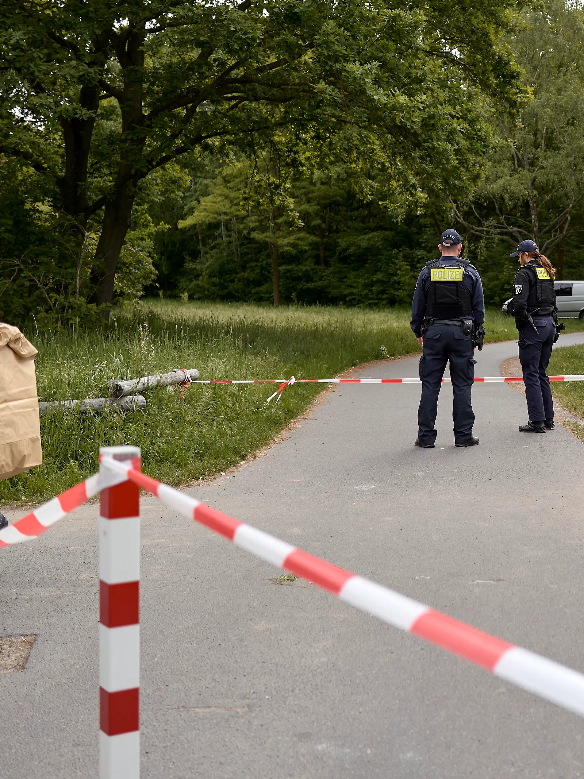 Einsatzkräfte der Polizei stehen hinter einer Absperrung an einem Weg im Stadtteil Gropiusstadt im Bezirk Neukölln, wo ein Polizist am frühen Morgen einen toten Säugling gefunden hat.