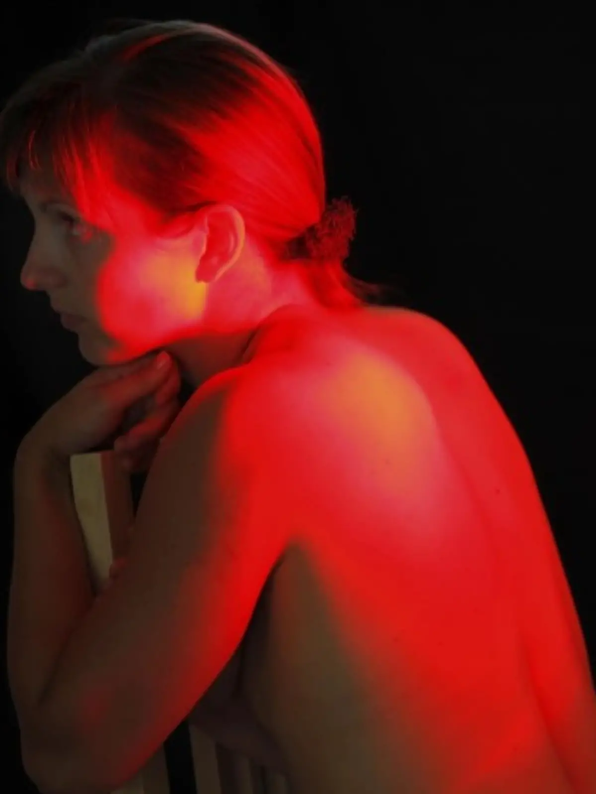 Frau sitzt mit nacktem Rücken vor einer Rotlichtlampe
