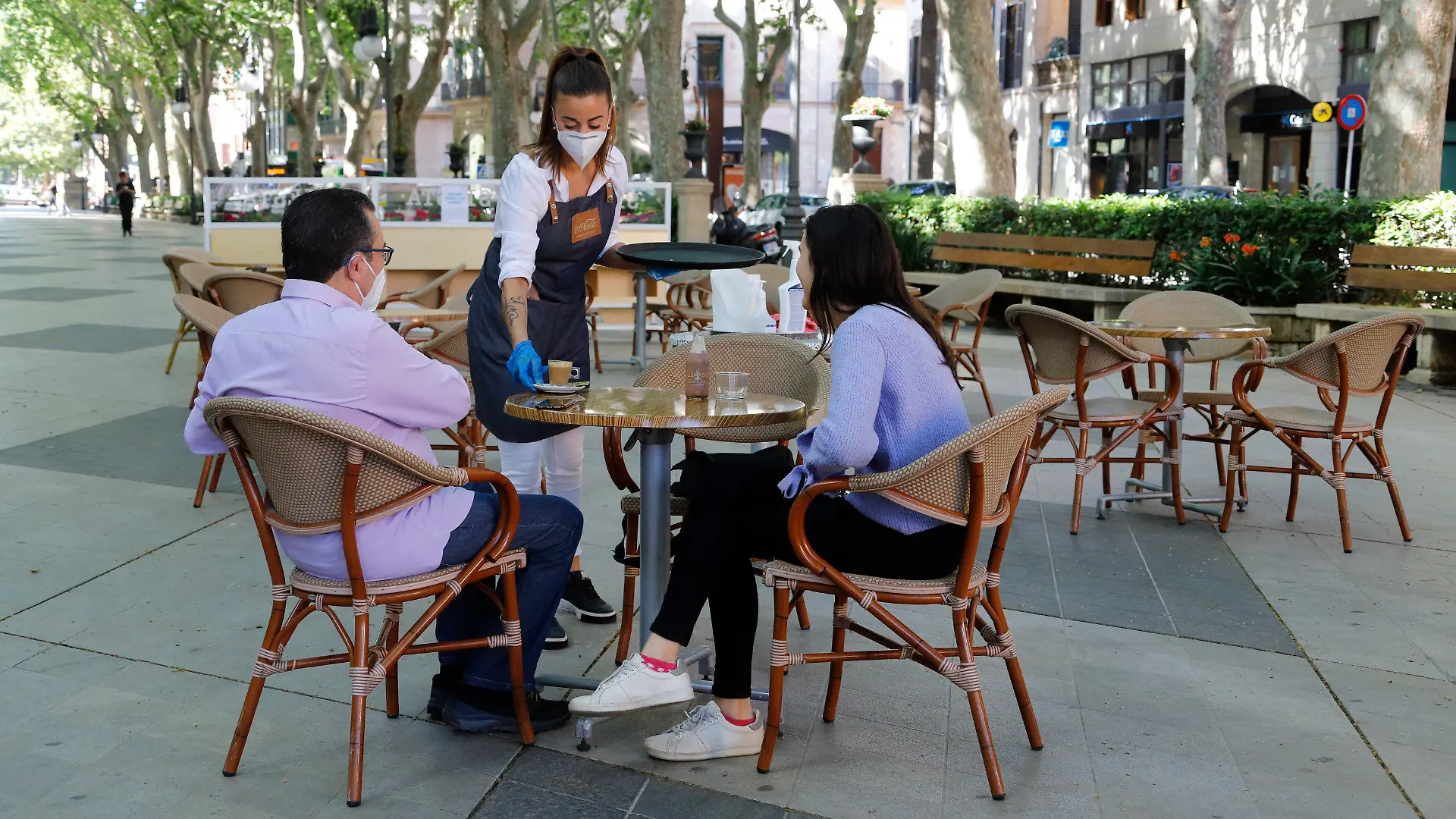 11.05.2020, Spanien, Palma: Am Tag der Wiedereröffnung serviert eine Kellnerin zwei Gästen auf der Terrasse einer Bar in Palma einen Kaffee. Ab Montag dürfen in der «Phase 1» der Lockerungen der Corona-Maßnahmen unter anderem Bars, Restaurants, Geschäfte, Bibliotheken und religiöse Kultstätten wieder eröffnen. Foto: Clara Margais/dpa +++ dpa-Bildfunk +++