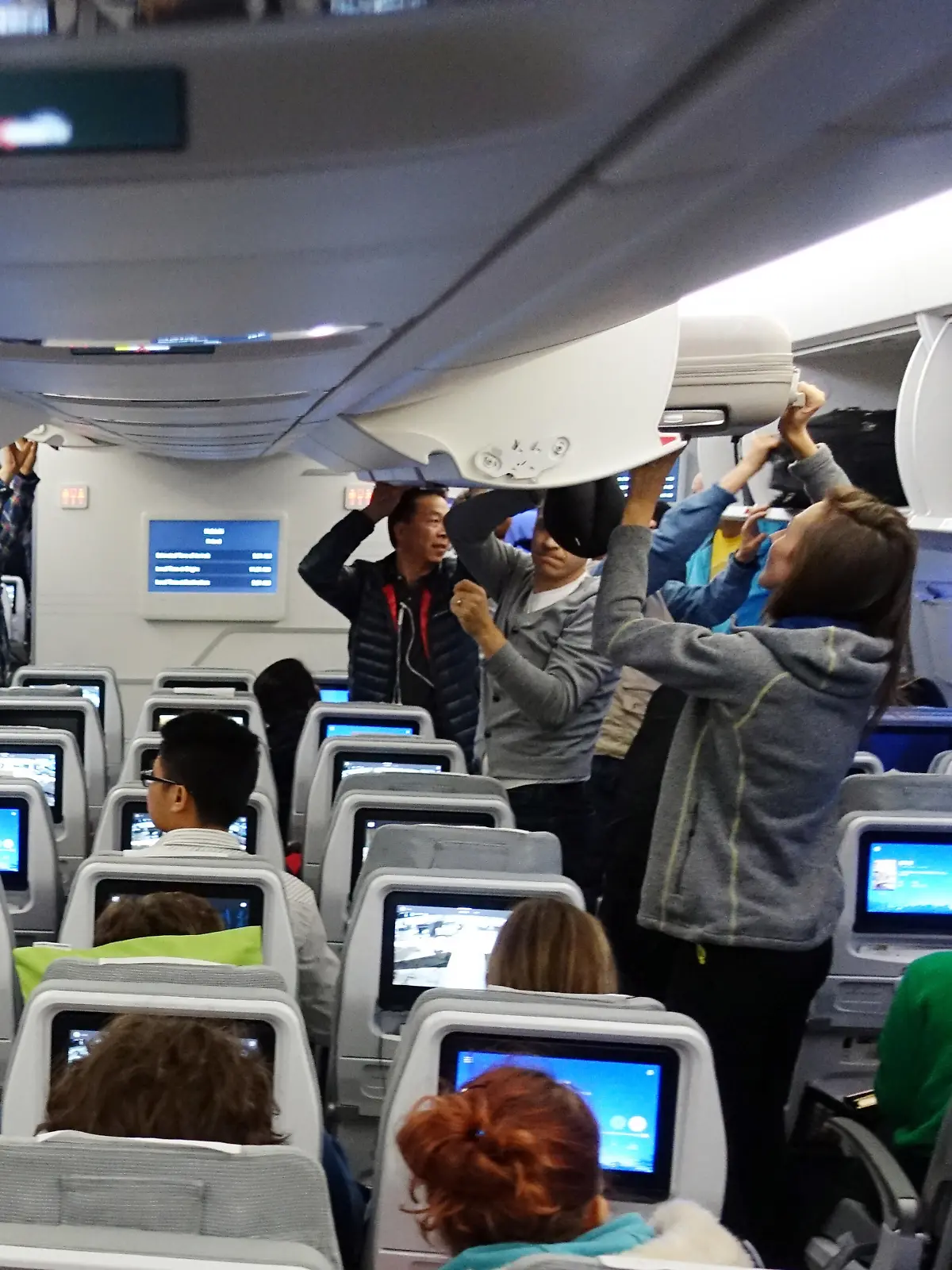 Menschen im Flugzeug holen ihr Handgepäck aus den Deckenfächern.