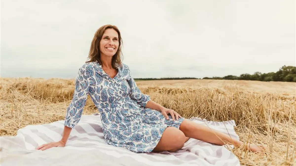 Ü50-Frau in einem geblümten Sommerkleid auf einer Wiese.